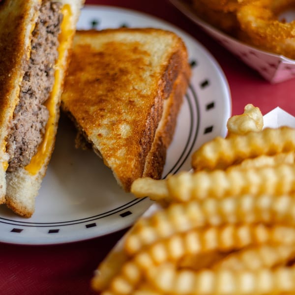A patty melt with melted cheese and a side of waffle fries on a red table.