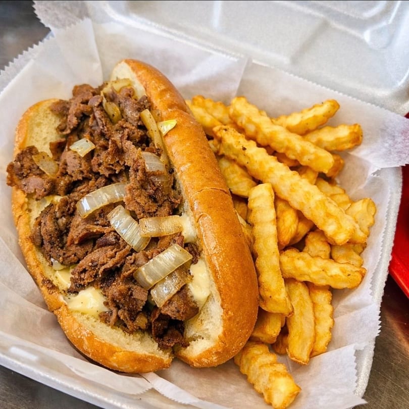 A Griffith's Drive-In cheesesteak with onions and crinkle-cut fries in a white takeout container.