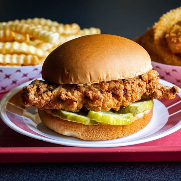 A crispy fried chicken sandwich with pickles on a bun, served with crinkle-cut fries.