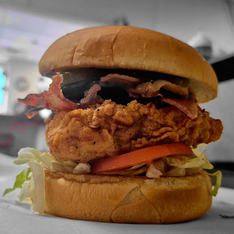 A crispy fried chicken sandwich with bacon, lettuce, and tomato on a bun from Griffith's Drive-In.