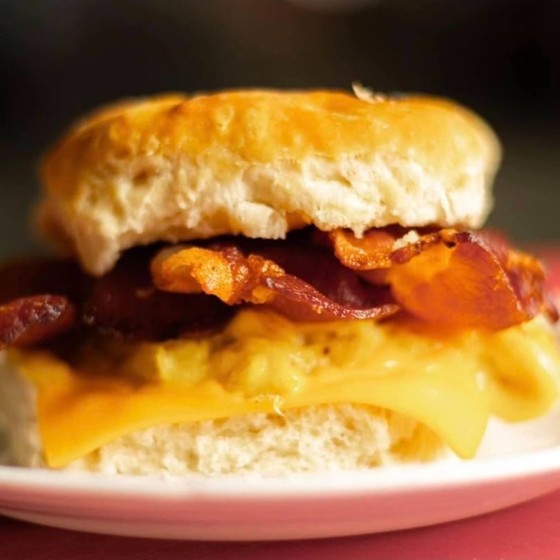 A close-up of a breakfast sandwich with bacon, egg, and cheese on a biscuit.
